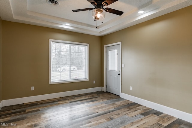 unfurnished room with hardwood / wood-style flooring, ceiling fan, and a tray ceiling