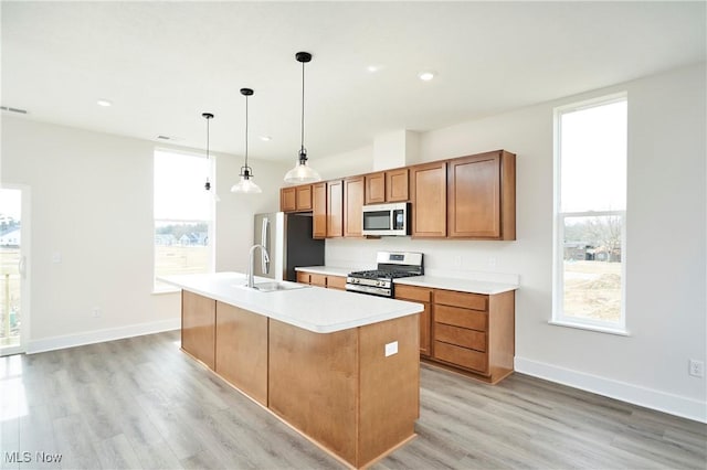 kitchen with an island with sink, brown cabinets, light wood-style floors, stainless steel appliances, and a sink