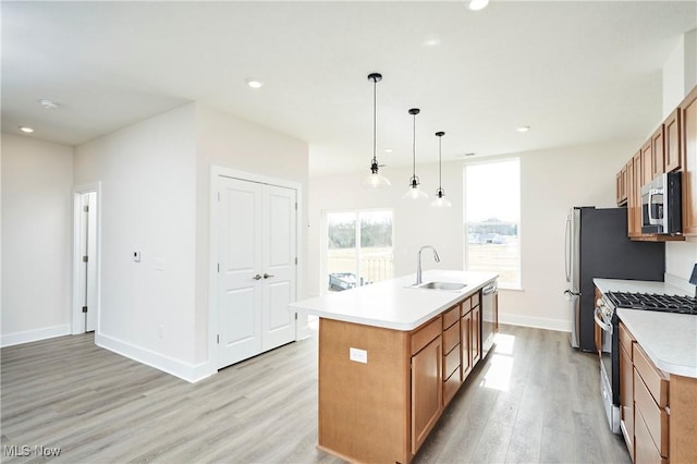 kitchen with brown cabinetry, a center island with sink, stainless steel appliances, and light wood-style floors