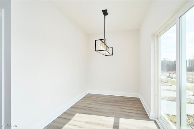 unfurnished dining area featuring baseboards, an inviting chandelier, and wood finished floors