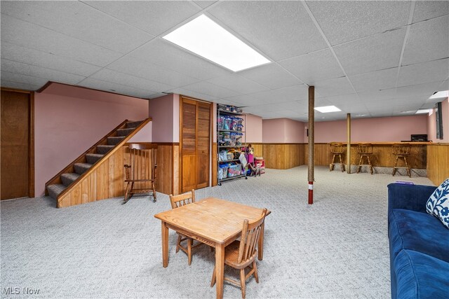 living room featuring a paneled ceiling, carpet flooring, and wooden walls