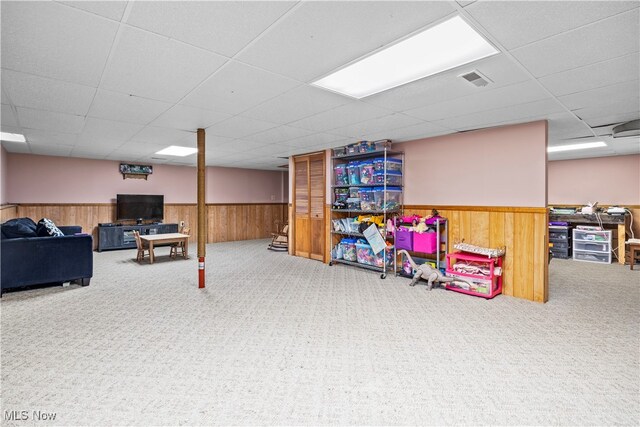 basement with a paneled ceiling, carpet flooring, and wood walls