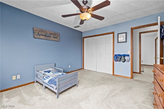 bedroom with ceiling fan, a textured ceiling, light carpet, and a closet