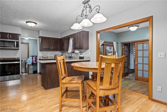 kitchen featuring dark brown cabinets, a textured ceiling, stainless steel appliances, pendant lighting, and light hardwood / wood-style flooring