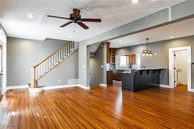 unfurnished living room with ceiling fan with notable chandelier, a textured ceiling, and hardwood / wood-style flooring