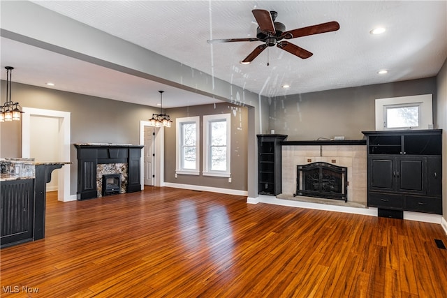 unfurnished living room with a tiled fireplace, a wealth of natural light, hardwood / wood-style floors, and a textured ceiling