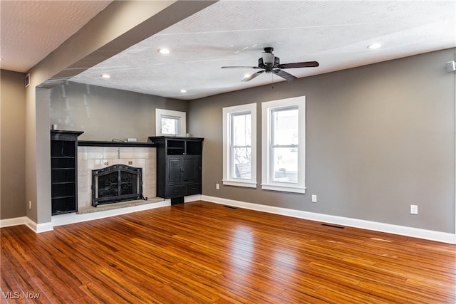 unfurnished living room featuring hardwood / wood-style floors, ceiling fan, a textured ceiling, and a tiled fireplace