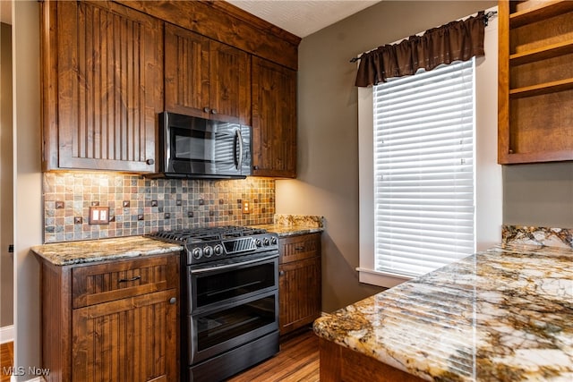 kitchen featuring decorative backsplash, light stone counters, wood-type flooring, and appliances with stainless steel finishes