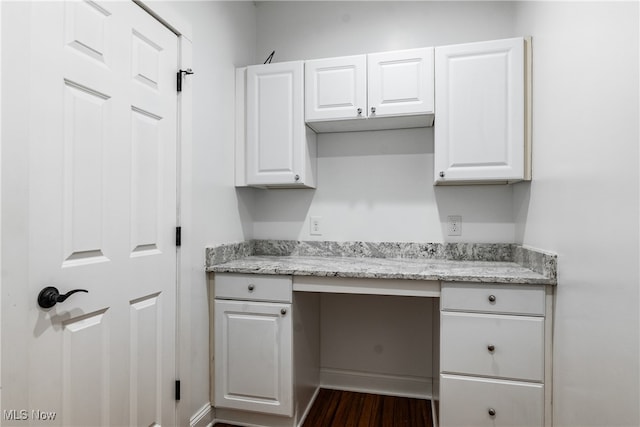 kitchen featuring dark hardwood / wood-style flooring, white cabinetry, light stone counters, and built in desk