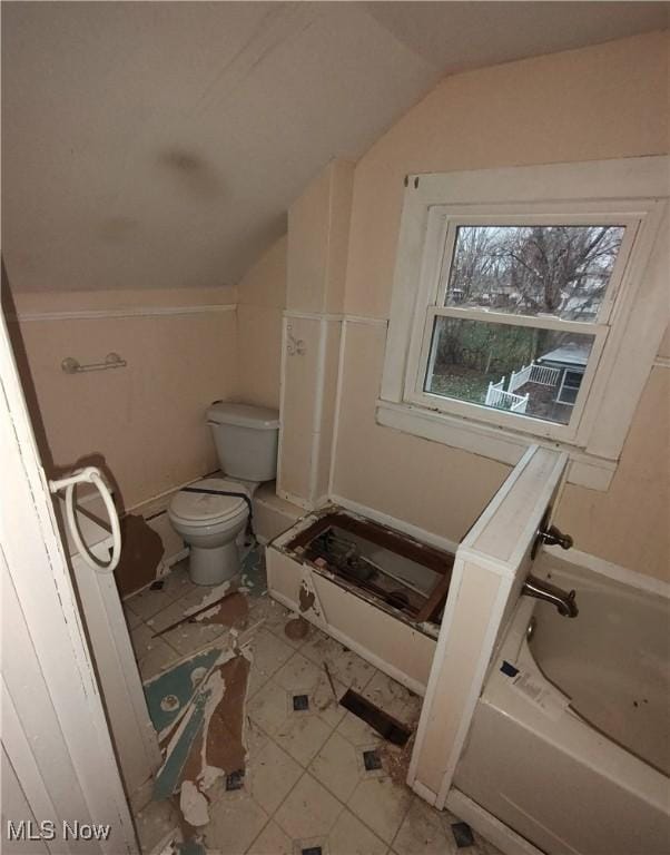 bathroom with toilet, tile patterned floors, vaulted ceiling, and a tub