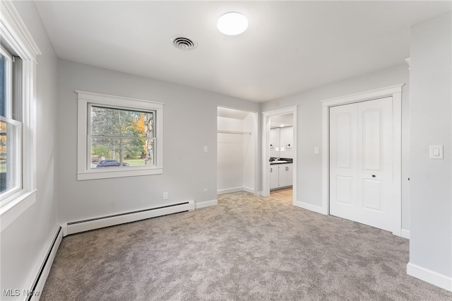 unfurnished bedroom featuring ensuite bath, multiple windows, light carpet, and a baseboard radiator