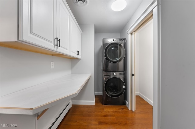 laundry room featuring cabinets, dark wood-type flooring, stacked washer and clothes dryer, and a baseboard heating unit