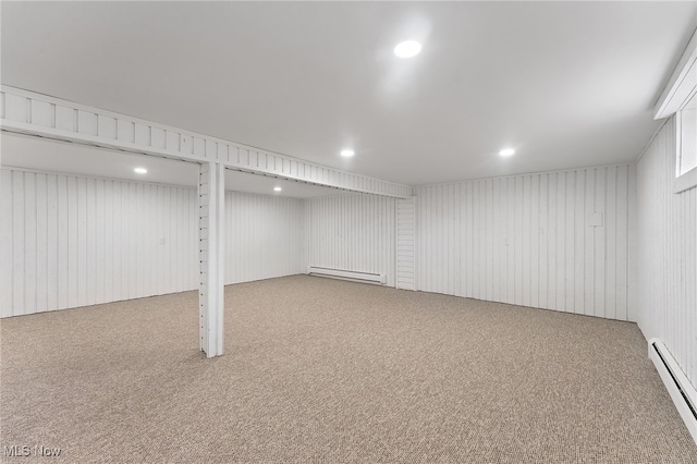 basement with wooden walls, carpet floors, and a baseboard heating unit