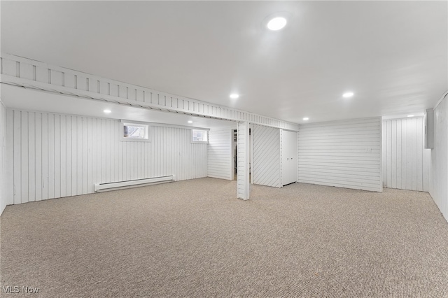 basement featuring wooden walls, light colored carpet, and a baseboard heating unit