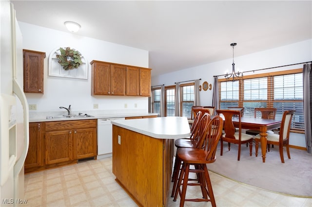 kitchen with white appliances, sink, a notable chandelier, a kitchen island, and hanging light fixtures