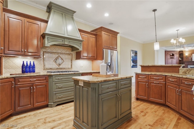 kitchen with premium range hood, hanging light fixtures, appliances with stainless steel finishes, a kitchen island, and light stone countertops