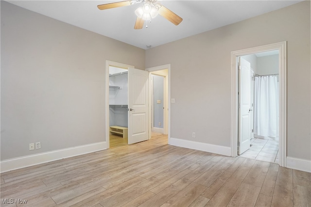 unfurnished bedroom featuring connected bathroom, a spacious closet, light wood-type flooring, a closet, and ceiling fan