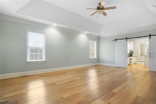 empty room featuring ceiling fan, a raised ceiling, crown molding, a barn door, and light wood-type flooring