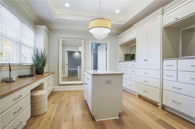 spacious closet featuring an inviting chandelier, a tray ceiling, built in desk, and light wood-type flooring