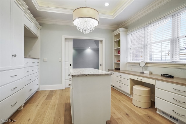 spacious closet featuring light hardwood / wood-style flooring, built in desk, a raised ceiling, and a chandelier