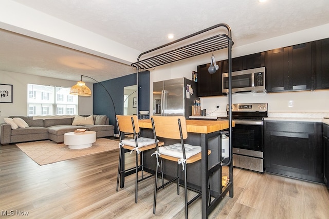 kitchen featuring wooden counters, a kitchen breakfast bar, light wood-type flooring, a textured ceiling, and stainless steel appliances