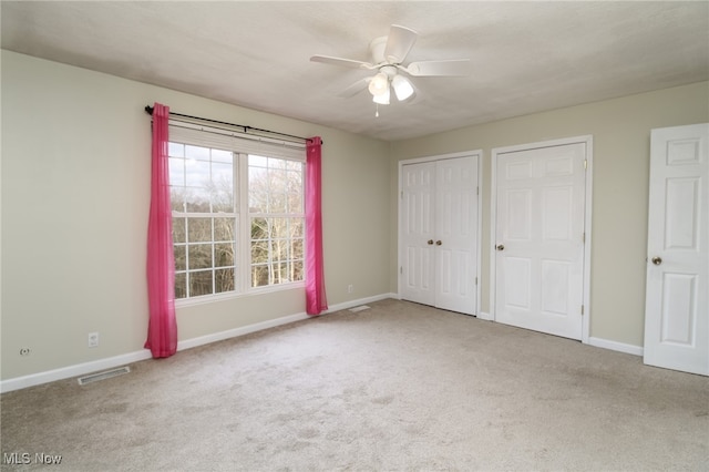 unfurnished bedroom with carpet flooring, two closets, and ceiling fan