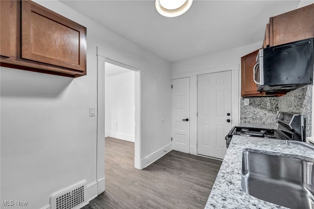 kitchen with sink, light stone counters, light hardwood / wood-style floors, decorative backsplash, and appliances with stainless steel finishes