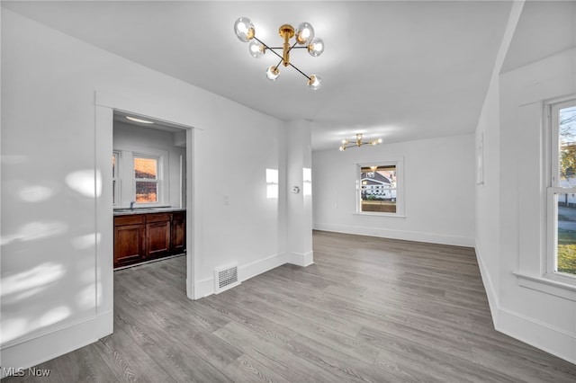 empty room with a chandelier, light wood-type flooring, and a wealth of natural light