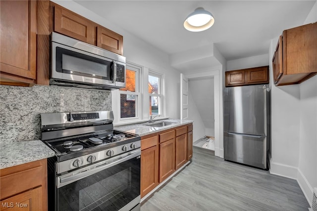 kitchen with light stone countertops, sink, light hardwood / wood-style floors, decorative backsplash, and appliances with stainless steel finishes