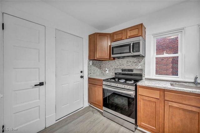 kitchen featuring backsplash, sink, light wood-type flooring, and appliances with stainless steel finishes