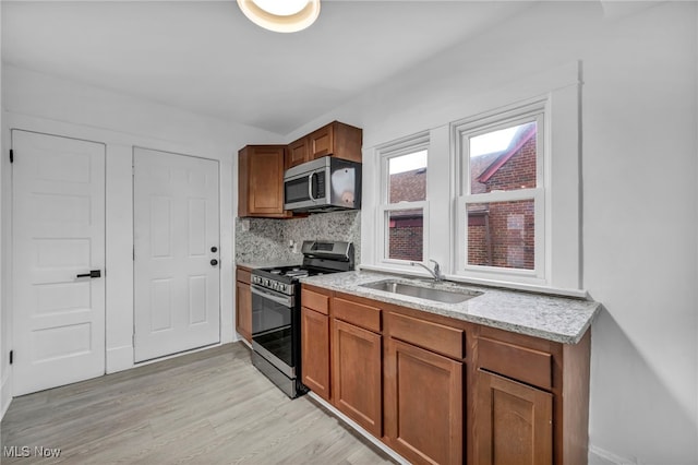 kitchen featuring sink, light stone counters, light hardwood / wood-style flooring, backsplash, and appliances with stainless steel finishes