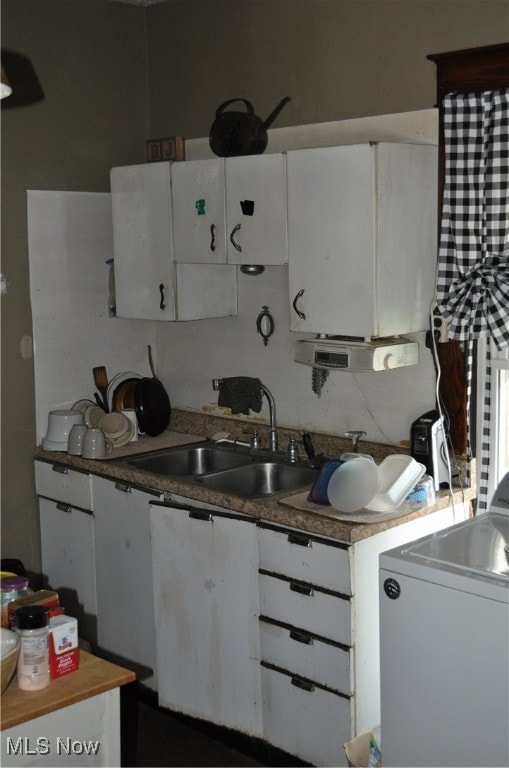 kitchen with white cabinets, washer / dryer, and sink