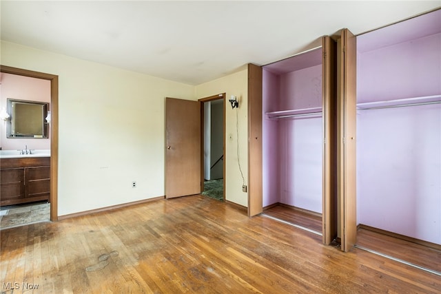 unfurnished bedroom featuring ensuite bathroom, hardwood / wood-style flooring, a closet, and sink