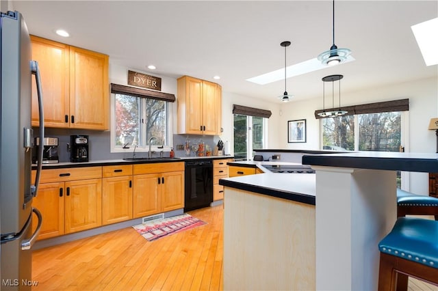 kitchen featuring dishwasher, sink, a skylight, stainless steel fridge, and decorative light fixtures