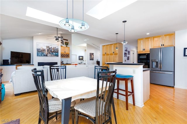 dining area with lofted ceiling with skylight, light hardwood / wood-style flooring, and ceiling fan