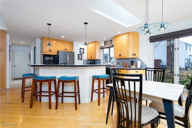 kitchen featuring stainless steel fridge, tasteful backsplash, black microwave, pendant lighting, and light hardwood / wood-style floors