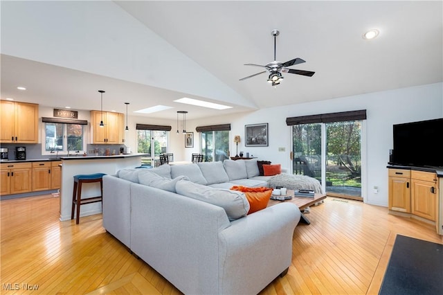 living room featuring a skylight, ceiling fan, high vaulted ceiling, and light hardwood / wood-style floors