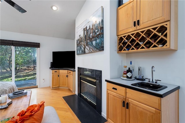 bar featuring sink, light brown cabinets, a premium fireplace, light hardwood / wood-style floors, and lofted ceiling