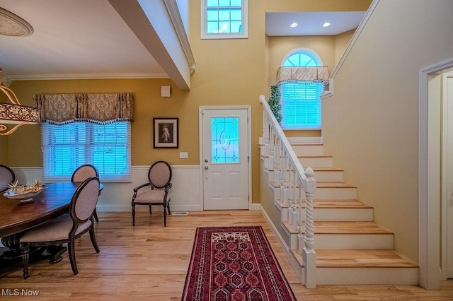 foyer featuring stairs, ornamental molding, wainscoting, and light wood-style flooring