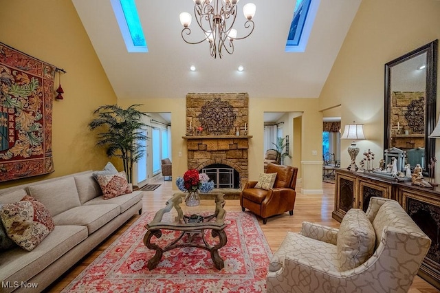 living room with high vaulted ceiling, a skylight, light wood-style floors, and a stone fireplace