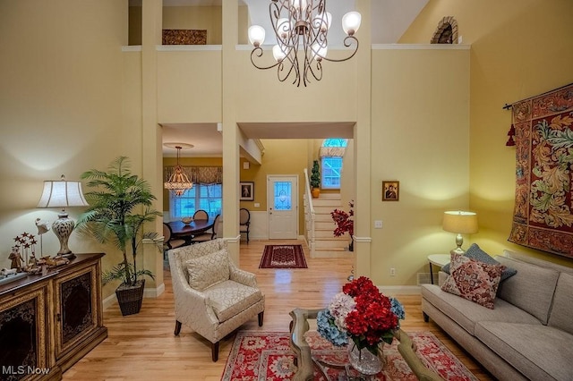 living room featuring baseboards, stairs, a high ceiling, light wood-style floors, and a notable chandelier