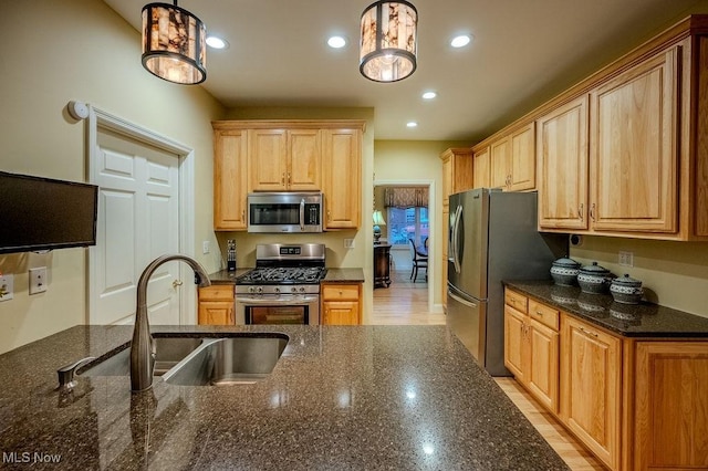 kitchen featuring recessed lighting, stainless steel appliances, a sink, hanging light fixtures, and dark stone countertops