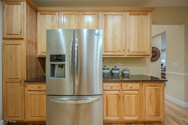 kitchen with stainless steel fridge with ice dispenser, light wood-style flooring, light brown cabinetry, dark stone countertops, and baseboards