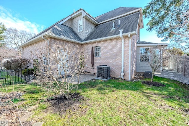 rear view of house with central AC unit, roof with shingles, fence, a yard, and brick siding