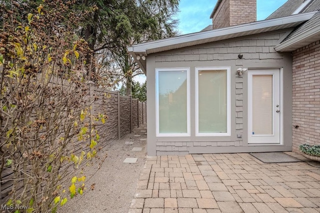 view of exterior entry with a patio area, a chimney, fence, and brick siding