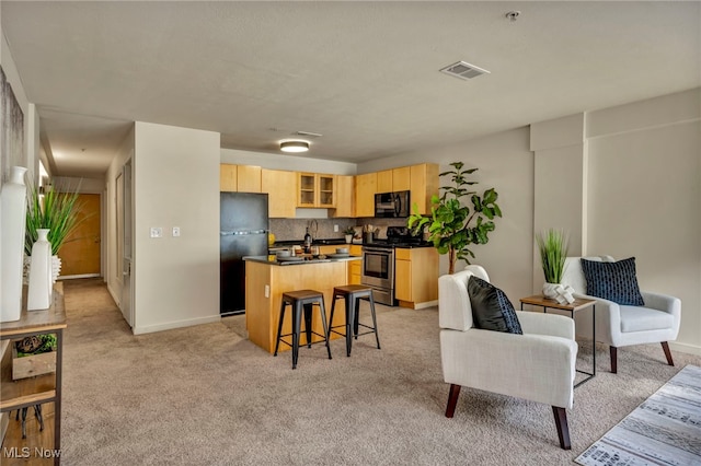 kitchen with an island with sink, light colored carpet, decorative backsplash, light brown cabinetry, and black appliances