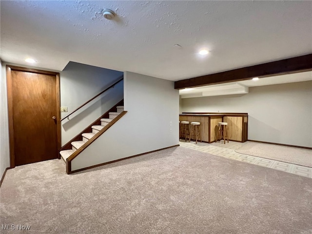 basement featuring a textured ceiling, light carpet, and bar