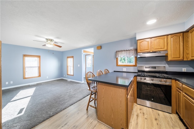 kitchen featuring stainless steel gas range, light hardwood / wood-style floors, a textured ceiling, a breakfast bar area, and a kitchen island