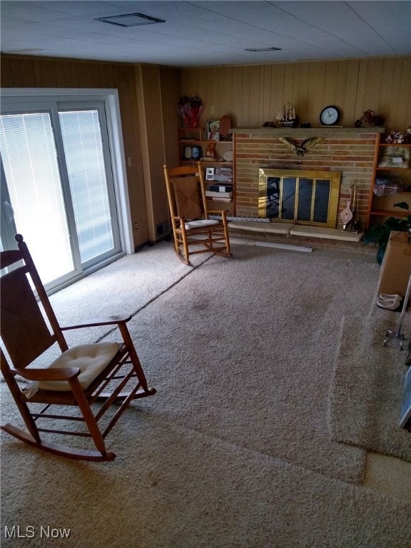 unfurnished living room with carpet floors, a brick fireplace, and wood walls