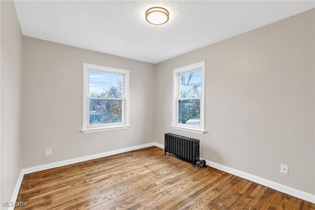 spare room featuring a wealth of natural light, radiator heating unit, and light wood-type flooring